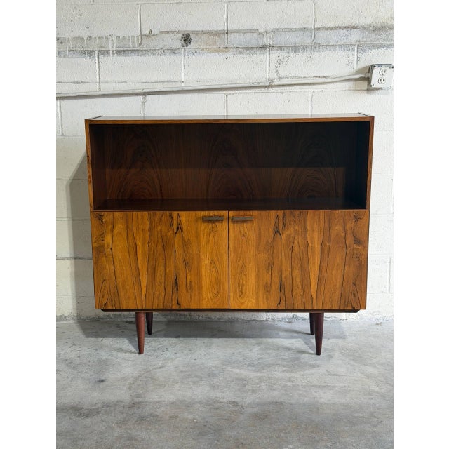 This elegant mid-sized Bookcase features an upper open display shelf sitting above a lower two-door storage cabinet. It is...
