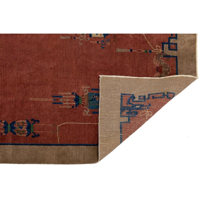 Antique 1920s Chinese wool rug featuring a rich red field framed by a chocolate brown border, adorned with intricate...