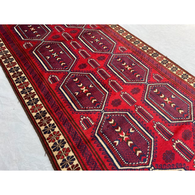 This Afghan hand-knotted runner rug features a beautiful octagonal geometric pattern woven in rich shades of red, navy,...