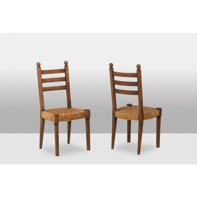 Set of 8 oak chairs with straw-seated seats; the backs are topped with decorative balls. Realzied in the 1950s. This piece...