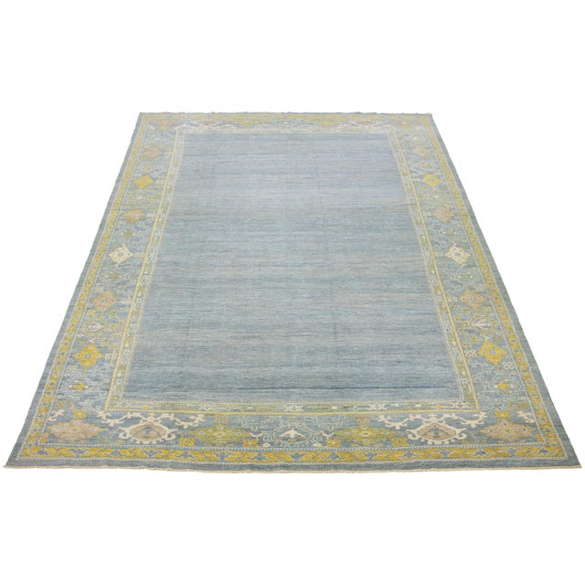 This hand-knotted wool rug features a light blue background with yellow and beige accents in a framed design. This rug...
