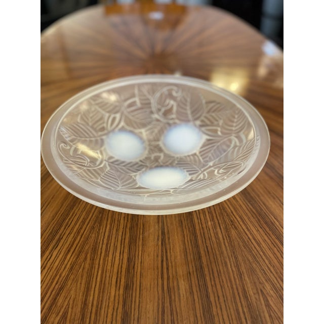 Round Art Deco-style valet tray featuring intricate engraved details of leaves and branches. The tray rests on three...