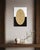 A softly patterned gold oval sits centered against a ground split cleanly in half, stark white above, deep black below....
