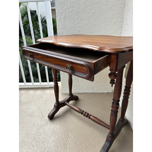 Charming vintage solid-wood side table featuring a scalloped edge tabletop, turned legs, and a single drawer with original...