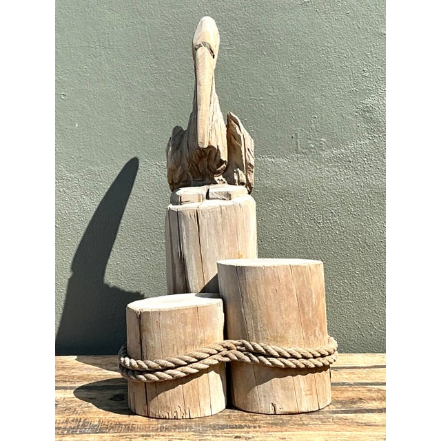 This exceptional vintage sculpture depicts a majestic pelican perched atop a trio of weathered dock pilings, capturing the...