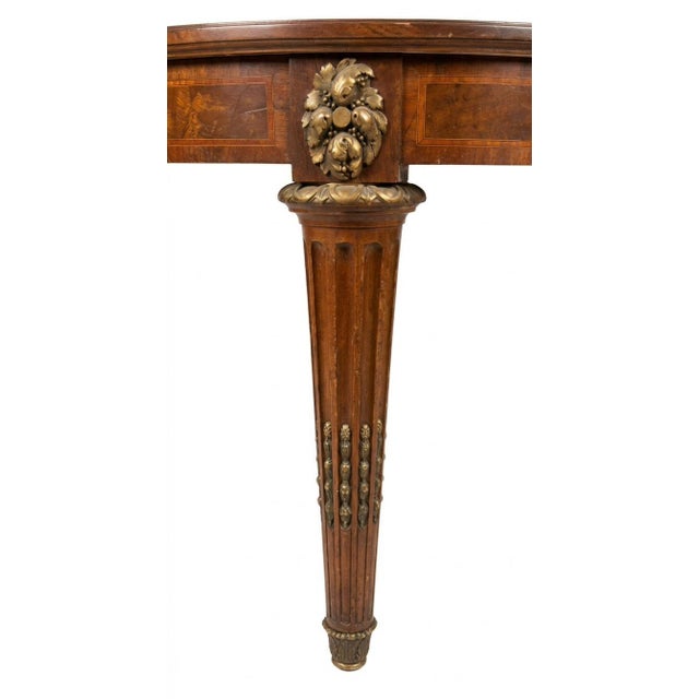It is characterized by its prominent fluted, tapered legs, a wide apron skirt, and distinctive decorative gilt-metal...