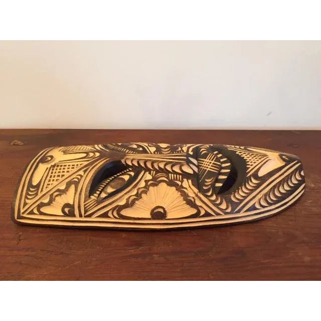 Exquisitely carved West African tribal mask; incised carved design areas are lighter; other areas are natural dark wood..