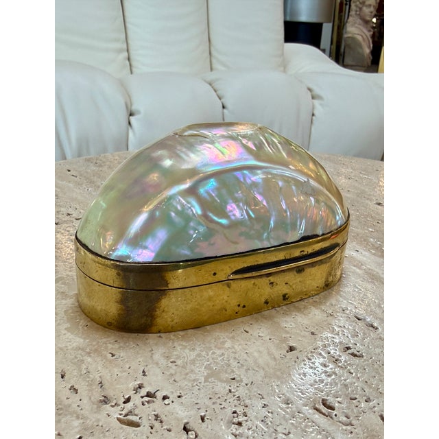 A striking decorative box featuring a large, naturally iridescent mother-of-pearl shell mounted within a polished brass...