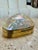 A striking decorative box featuring a large, naturally iridescent mother-of-pearl shell mounted within a polished brass...