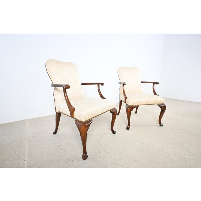 Pair of Baker Furniture Queen Anne style armchairs crafted in solid mahogany, featuring elegant cabriole legs, carved knee...