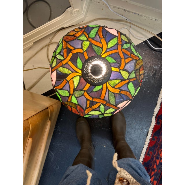 This vintage lamp's primary visual feature is the vivid floral design of the stained glass shade, finely hand-wrought;...