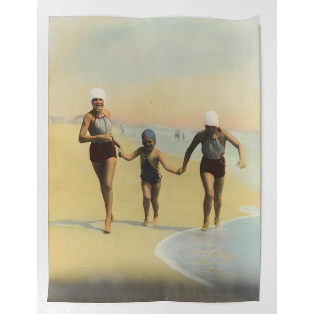 Early 20th century colortone advertising photograph of two women and a young girl in swimsuits runningalong the beach....