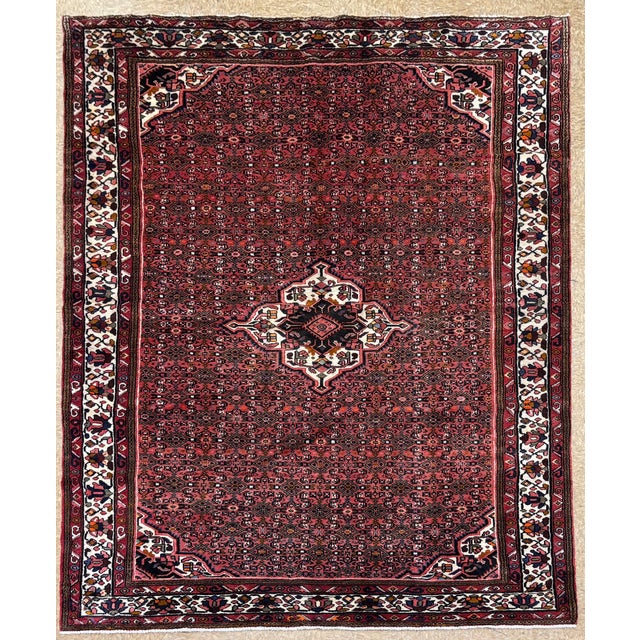 Hand-knotted rug from the Hamadan region of western Iran, featuring a small central medallion set within a densely...