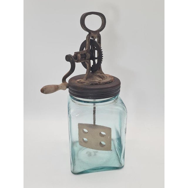 An original 3-liter hand-cranked butter churn, made of thick glass with a distinctive blue-green tint, equipped with a...
