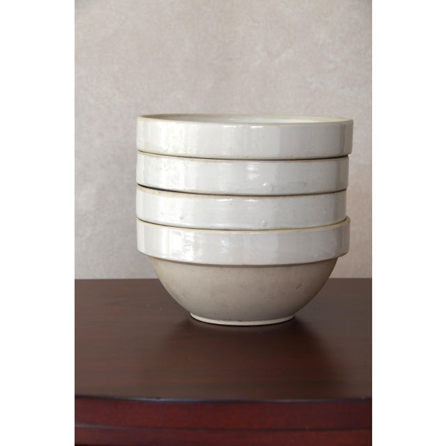 A traditional French ironstone bowl in a creamy off-white glaze, with a wide flat rim, slightly rounded body and footed...