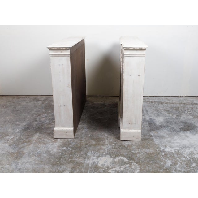 A pair of English Neoclassical style painted pine breakfront shelves from the 19th century, with dentil molding, carved...