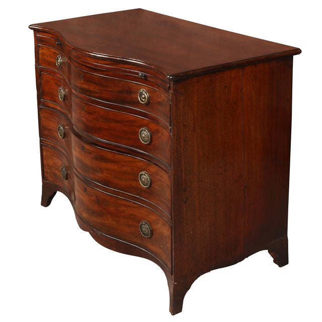 A classic bowfront mahogany chest features four spacious graduated drawers, each fitted with a pair of round brass pulls...