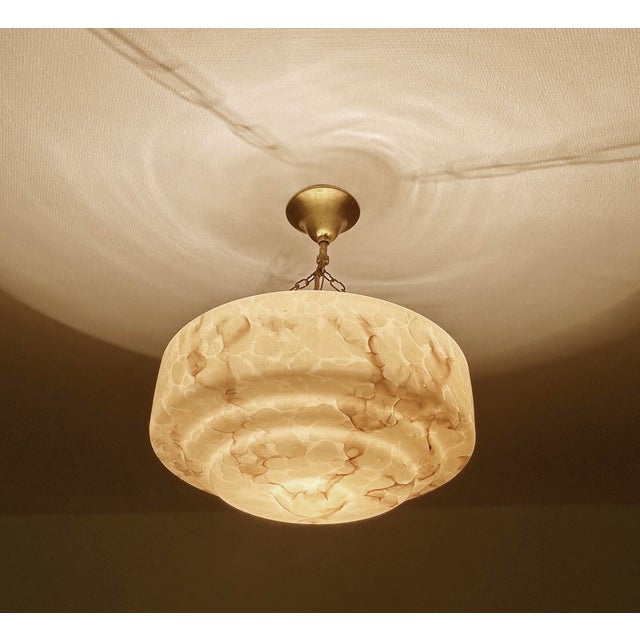 Art Deco pendant light from the 1930s, stepped salmon pink mottled glass shade with darker veins, mounted on a burnished...