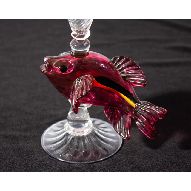 An art glass champagne flute by the American glass artist Ann Welch. Signed to the underside, the glass has a red fish...