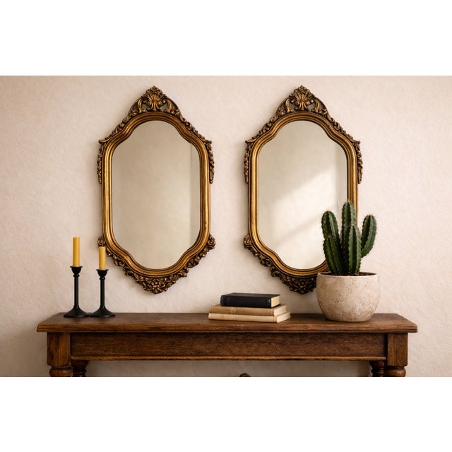 A striking pair of vintage Hollywood Regency wall mirrors featuring richly detailed gilt frames with elegant Rococo-...