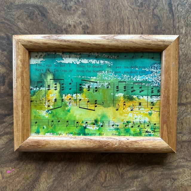 This one-of-a-kind piece features an abstract watercolor landscape painted directly over vintage sheet music. The vibrant...