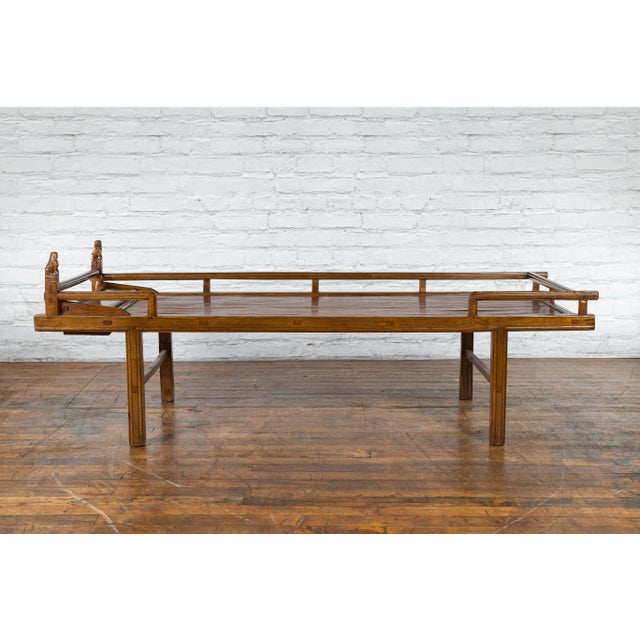 A Chinese Qing Dynasty period elm wood daybed from the 19th century, with carved foo dog guardian lions, bamboo slats and...