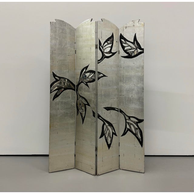A decorative four-panel folding screen featuring a luminous silver-leaf finish accented by bold, abstract botanical motifs...
