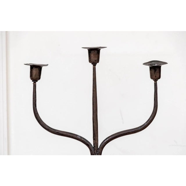 A tall, antique wrought iron three light floor candle stand with a tightly twisted shaft and a tripodal base with scrolled...