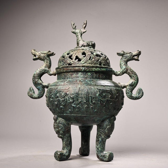 This is a cast bronze tripod censer or incense burner, featuring a domed lid topped with a seated deer finial. The lid is...