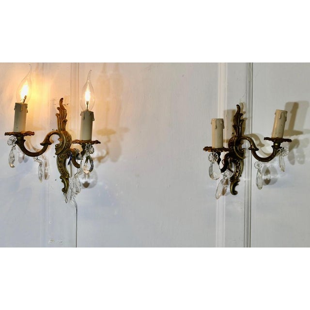 A pair of French Brass Twin Wall Lights The lights are in the classical style, hung with crystal lustres, they are in...