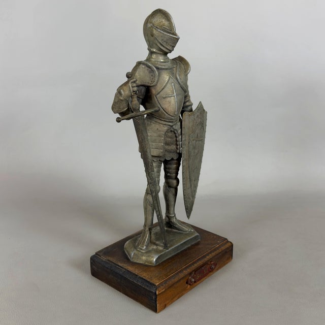 A striking and massive tabletop sculpture depicting a medieval knight in full armor with a sword and crossed shield,...