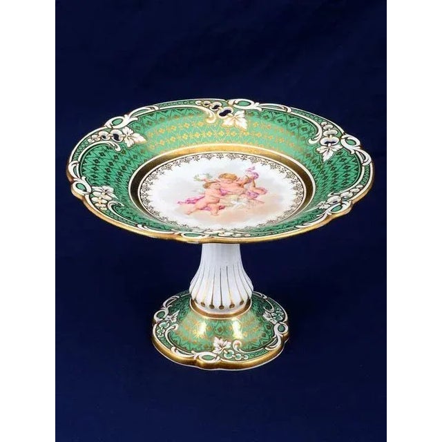 Antique French hand painted porcelain compote with cherubs, green border and gilt rim on scalloped column with a green...