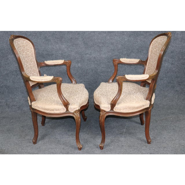 This attractive pair of French Louis XV-style armchairs, dating to approximately the 1940s, displays the graceful curves,...