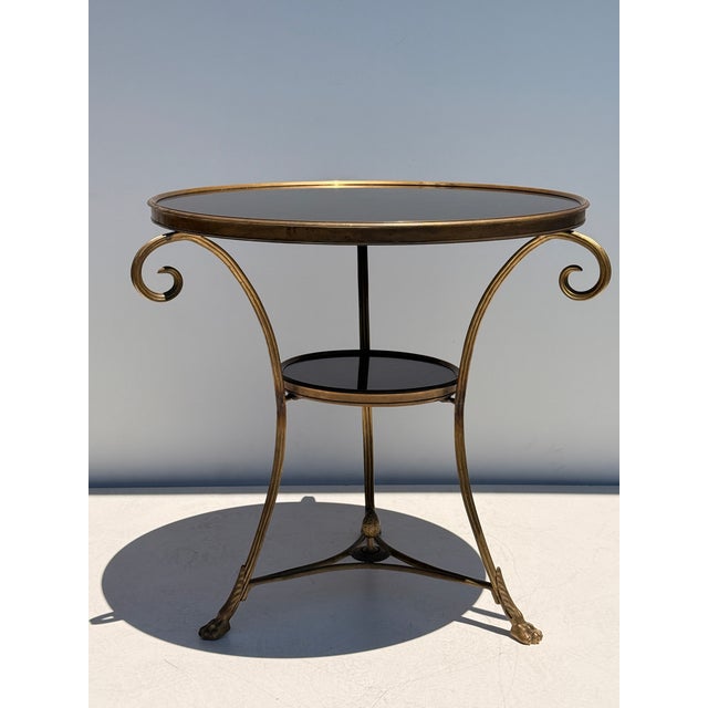 Patinated brass and black granite French style round Gueridon table with cast lion paw feet and center finial.