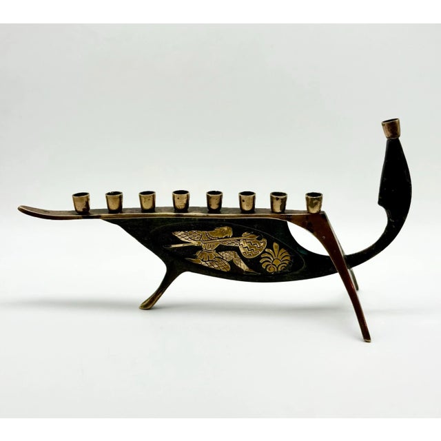 This striking mid-century brass menorah features a sculptural boat silhouette with elegant Damascene-style etching on both...