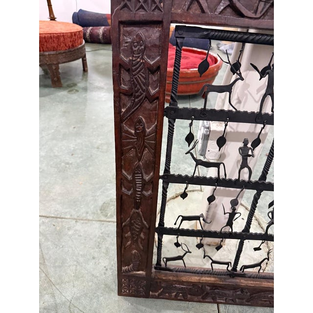 This striking handcrafted wall panel features a richly carved wooden frame surrounding an intricate wrought iron grille...