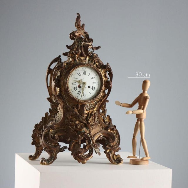 Gilded bronze table clock with leaf scroll and plant motifs. Enamelled metal dial with Roman numerals and perforated...