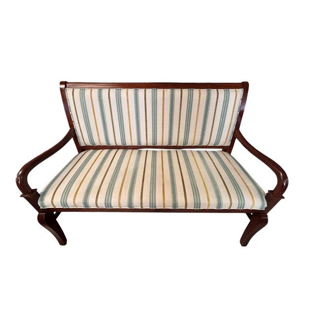 Elegant vintage Regency-style upholstered settee featuring a warm mahogany-finished wood frame, gracefully curved open...