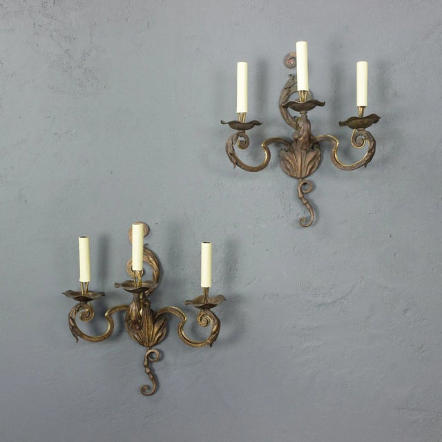 A charming pair of French wrought iron three-arm sconces dating to the 1920s, hand-forged in the Louis XV taste. Crafted...
