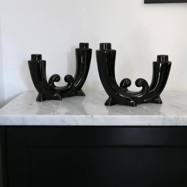 A superb pair of glossy black ceramic candlesticks with a fluid and symmetrical design. Their double-volute shape resting...