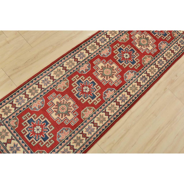A tribal Caucasian Kazak runner hand-knotted with fine wool on a cotton foundation. This rug features geometric medallions...
