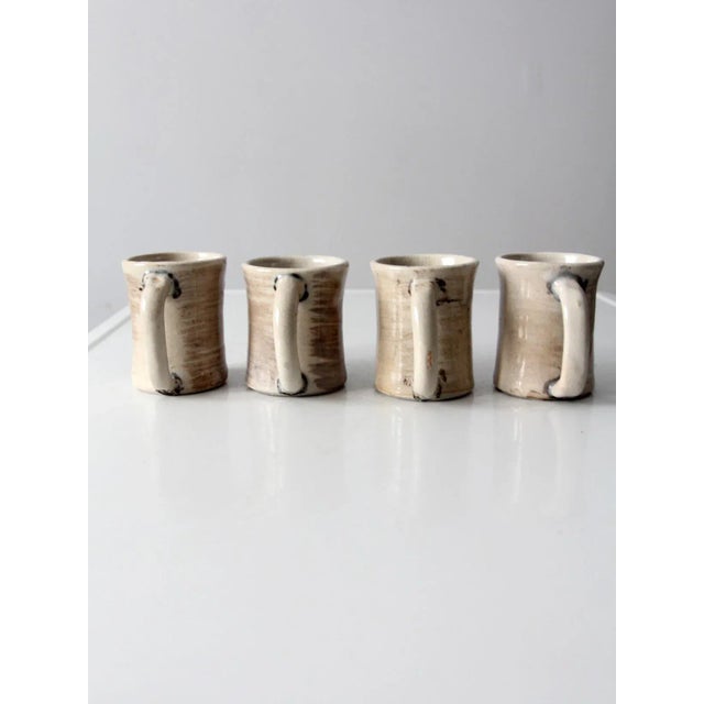 A set of four vintage studio pottery mugs, each signed by the artist with the initials JP. The handcrafted ceramic mugs...