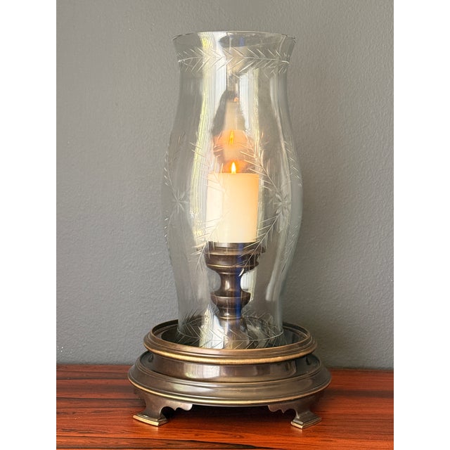 Patinated brass hurricane candle holder by Chapman. Glass hurricane is 7.5” diameter and 18” tall and decorated by...