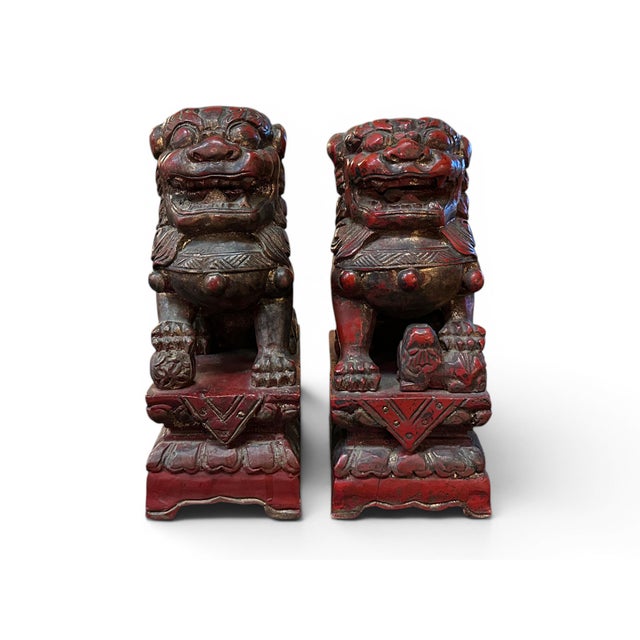 A pair of carved wood Chinese foo lions. Red coloring with traces of gilding. Appears to be a male and female. The taller...