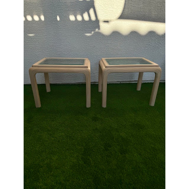 A beautiful pair of vintage rattan waterfall side tables with glass top inserts. These timeless tables have a clean...