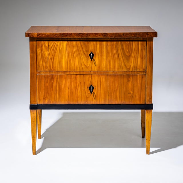 Two-drawer Biedermeier chest of drawers veneered in cherrywood, with ebonized details and a rootwood-veneered top. The...