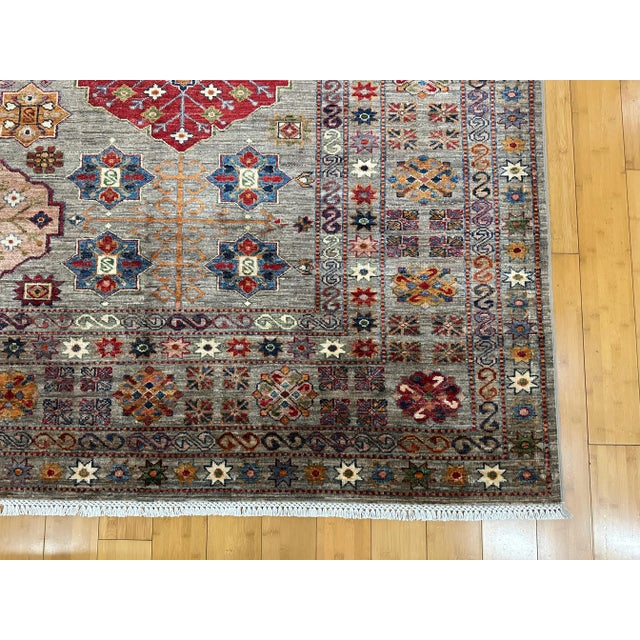 This 9x12 handmade Afghan Super Kazak rug features a vibrant tribal design with bold geometric medallions and star motifs...