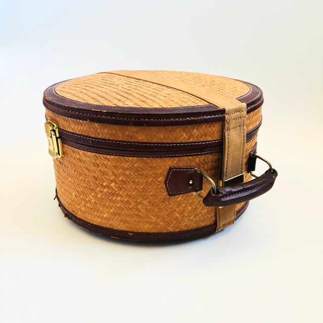 A vintage circular wicker suitcase. Features brass hardware, brown leather trim, and a leather handle. The interior is...