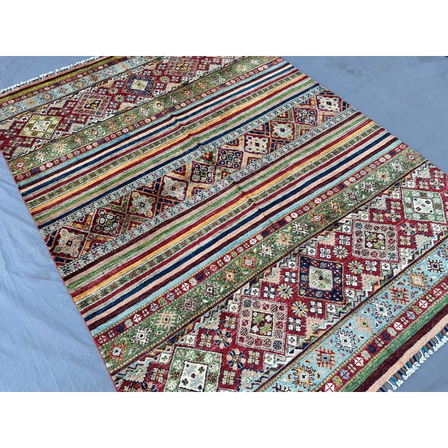 This hand-knotted Super Kazak rug alternates bold rows of diamond medallions in burgundy, green, and ivory with narrow...