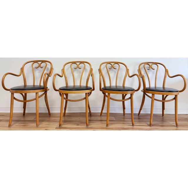 Classic set of four mid century bentwood dining chairs with rounded arms and curved backs. Solid wood frames feature black...